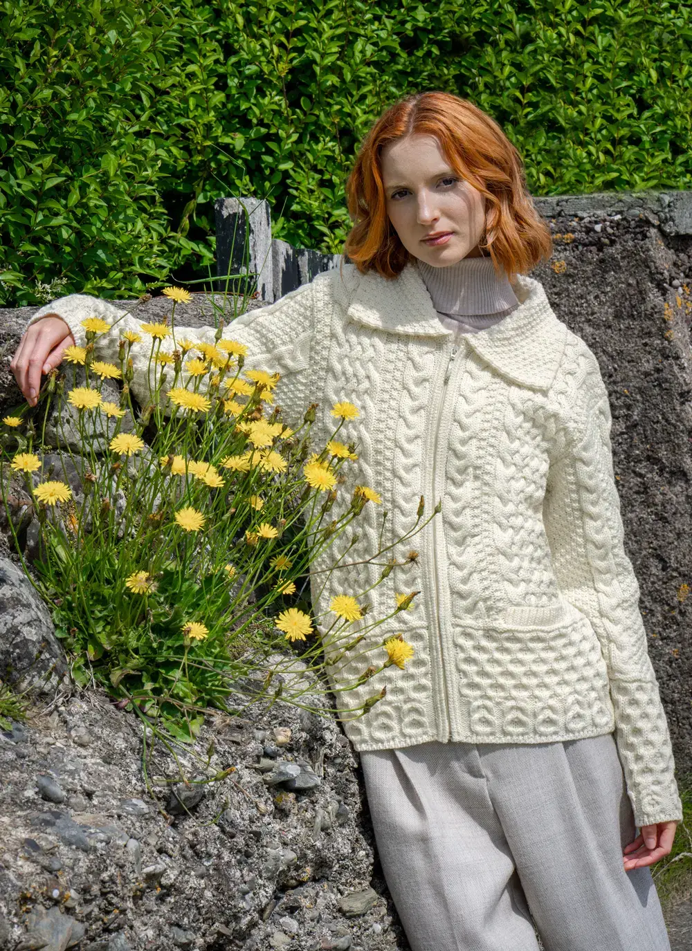 Red haired model in front of yellow flowers in Grace Full Zip Aran Cardigan in Natural